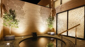 A tranquil indoor pool area with a stone edge, surrounded by walls with a textured pattern and potted plants. - Nemu Resort Hotel Nemu (Shima)