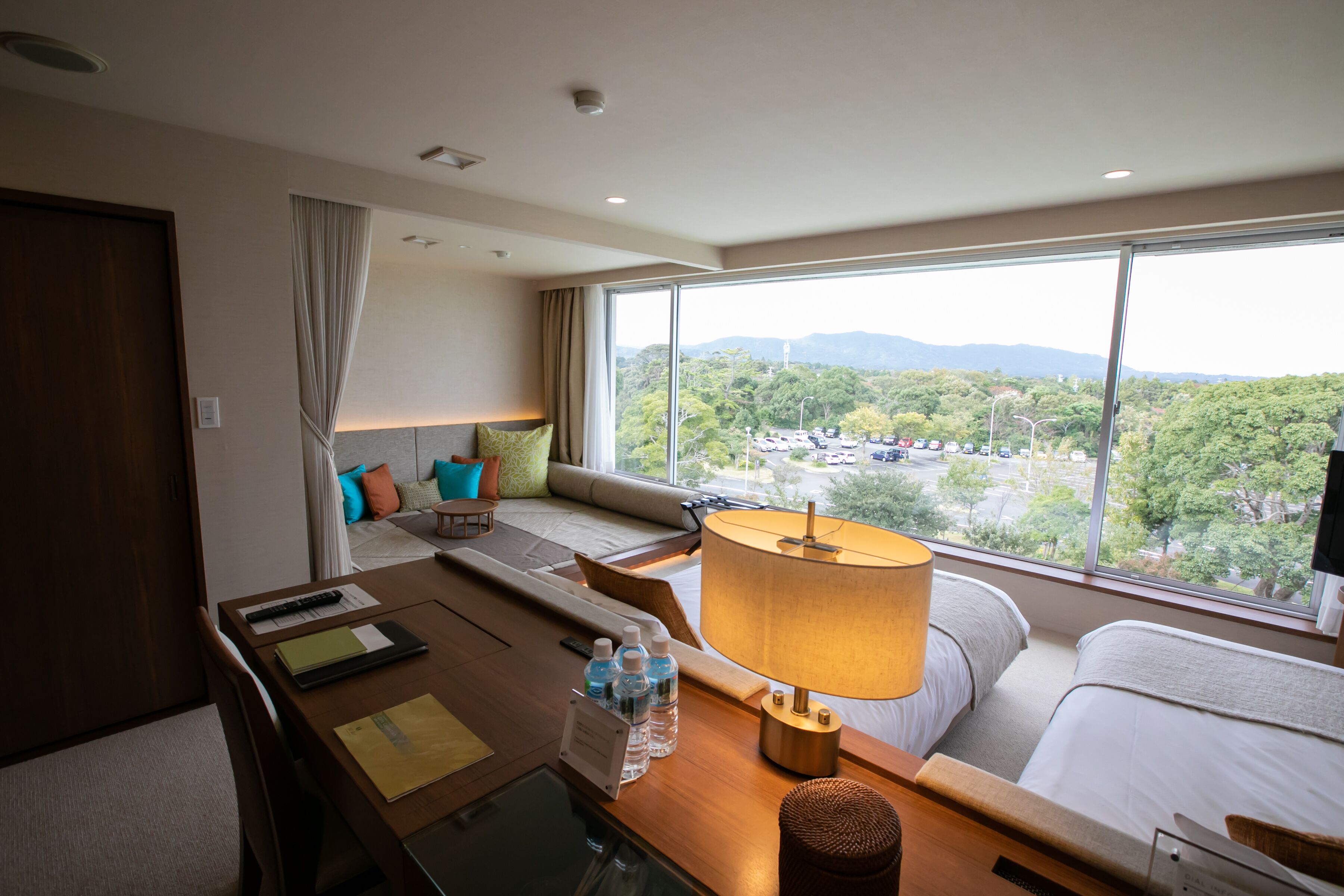 Una habitación de hotel con un ventanal grande, un sofá, una mesa con lámpara y una cama.