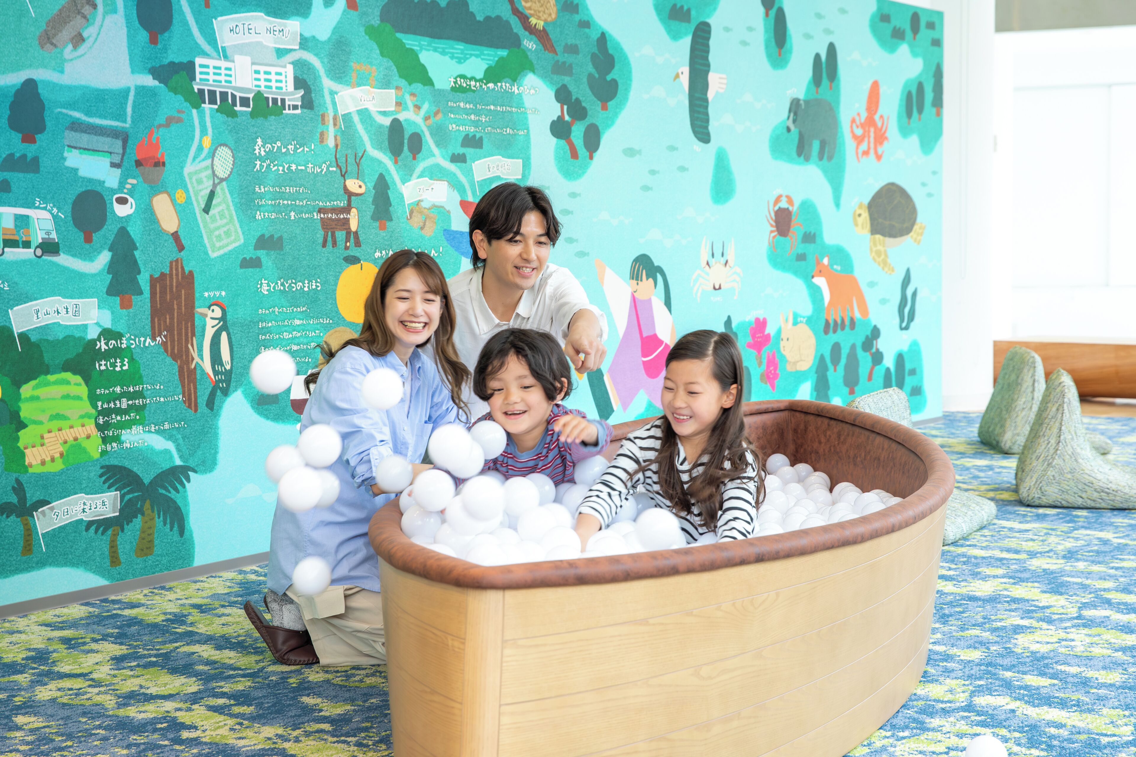 A group of people sitting in a wooden ball pit with a colorful mural in the background.