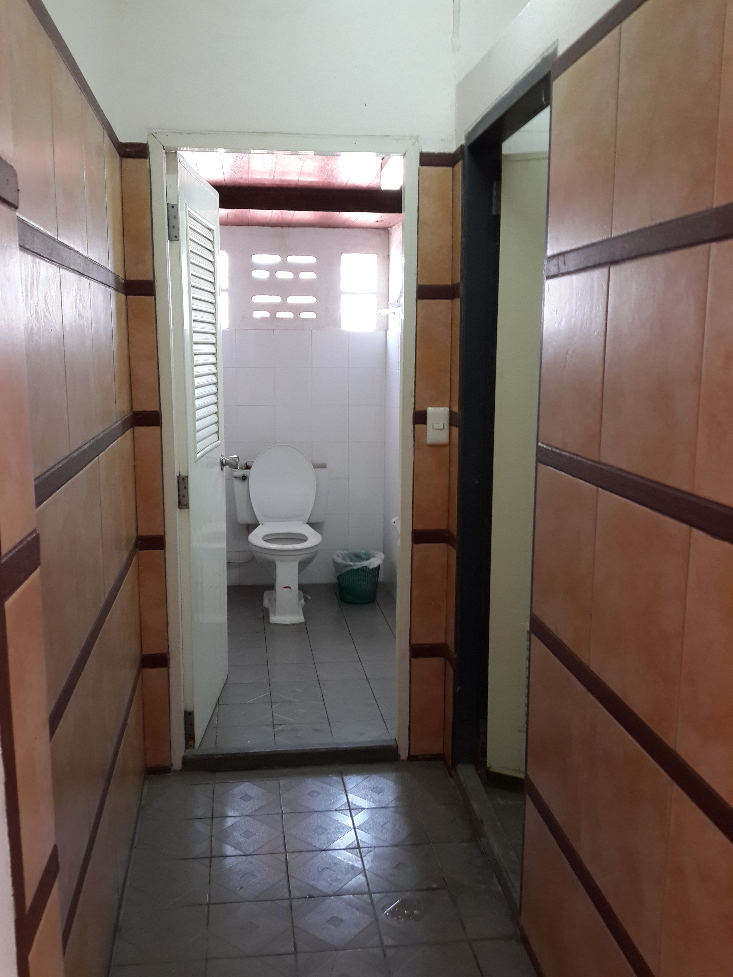 A narrow hallway leading to a bathroom with a toilet and a trash bin.
