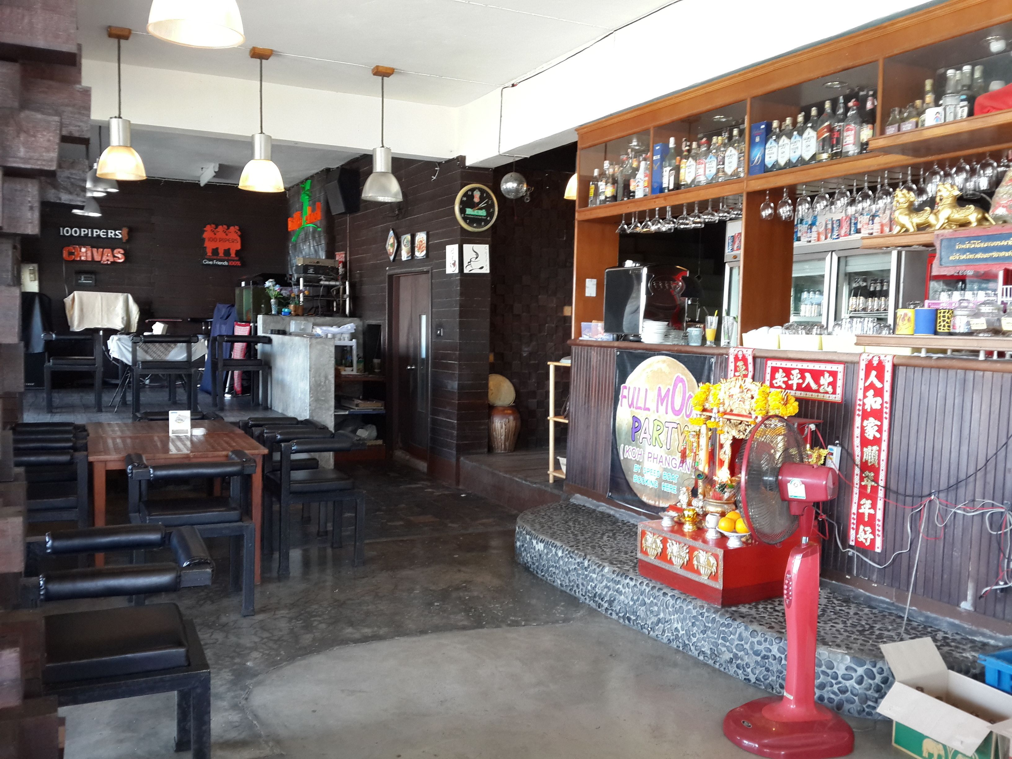 Een restaurantinterieur met een bar, tafels, stoelen en hangende lampen.