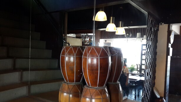 A set of wooden drums stacked on a counter, a staircase in the background, and hanging pendant lights. - Coffee Island - Hostel (Koh Samui)