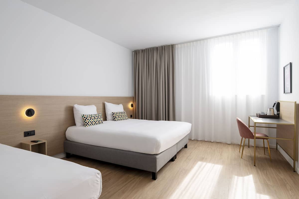 A modern hotel room with a large bed, a desk, and a chair.