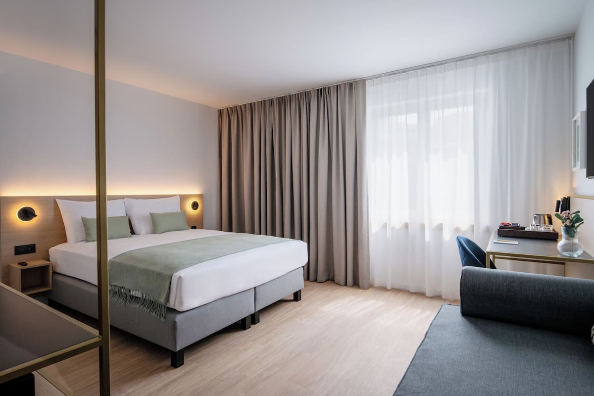 A modern hotel room with a large bed, bedside tables, a desk, and a chair.