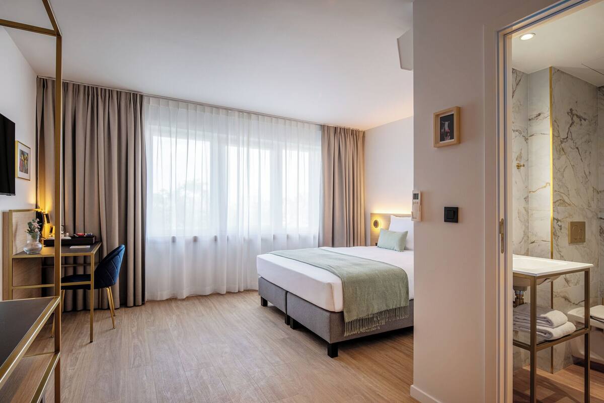 A hotel room with a bed, a desk with a chair, a TV, and a bathroom with a marble wall.