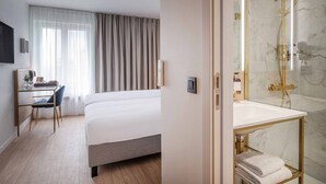 A hotel room with a bed, a desk with a chair, a shower with a marble wall, and a bathroom with a sink and towel rack. - Jill Hotel Brussels (Brussels)