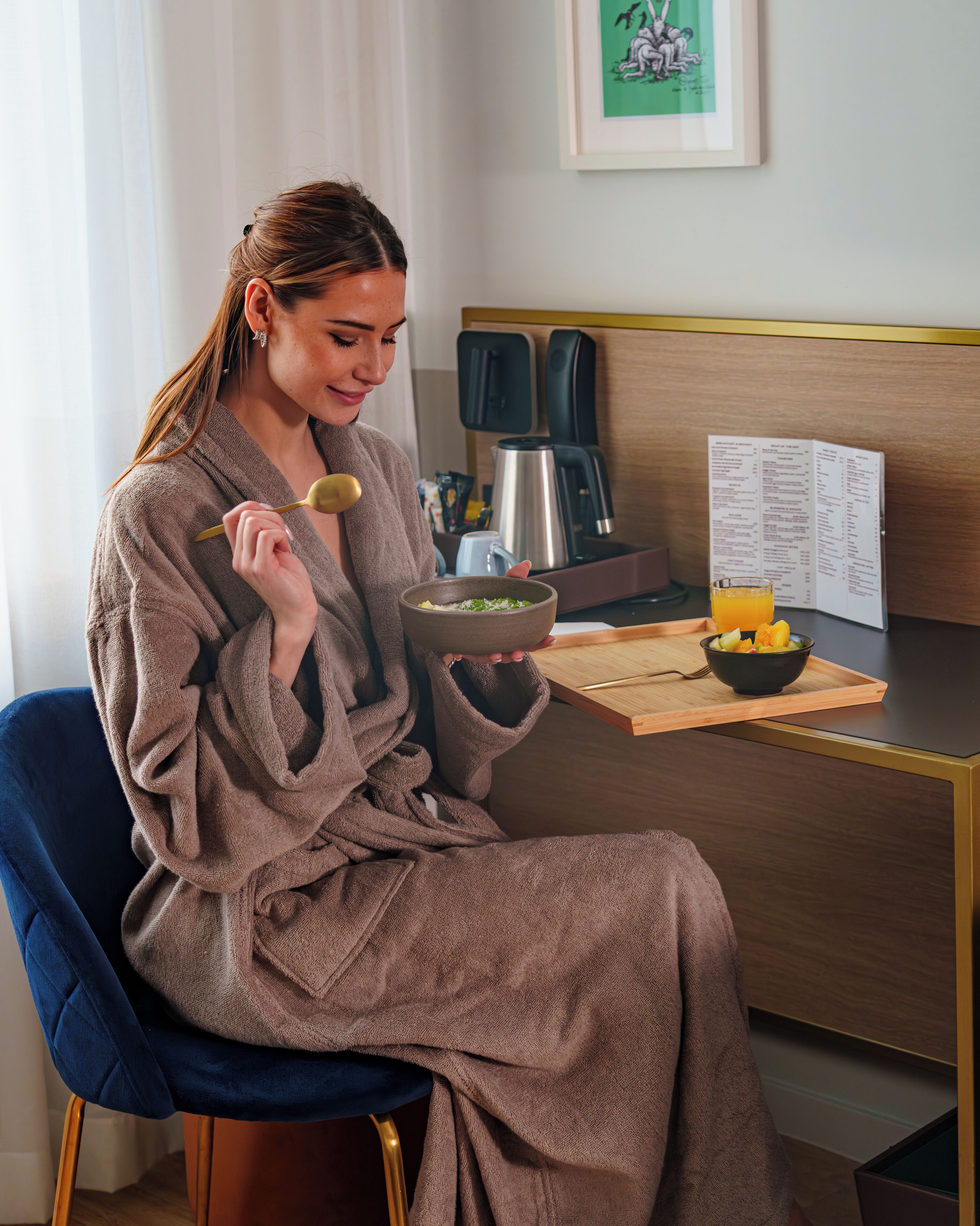 A person in a robe sitting at a wooden table with a bowl of food and a tray with fruit.