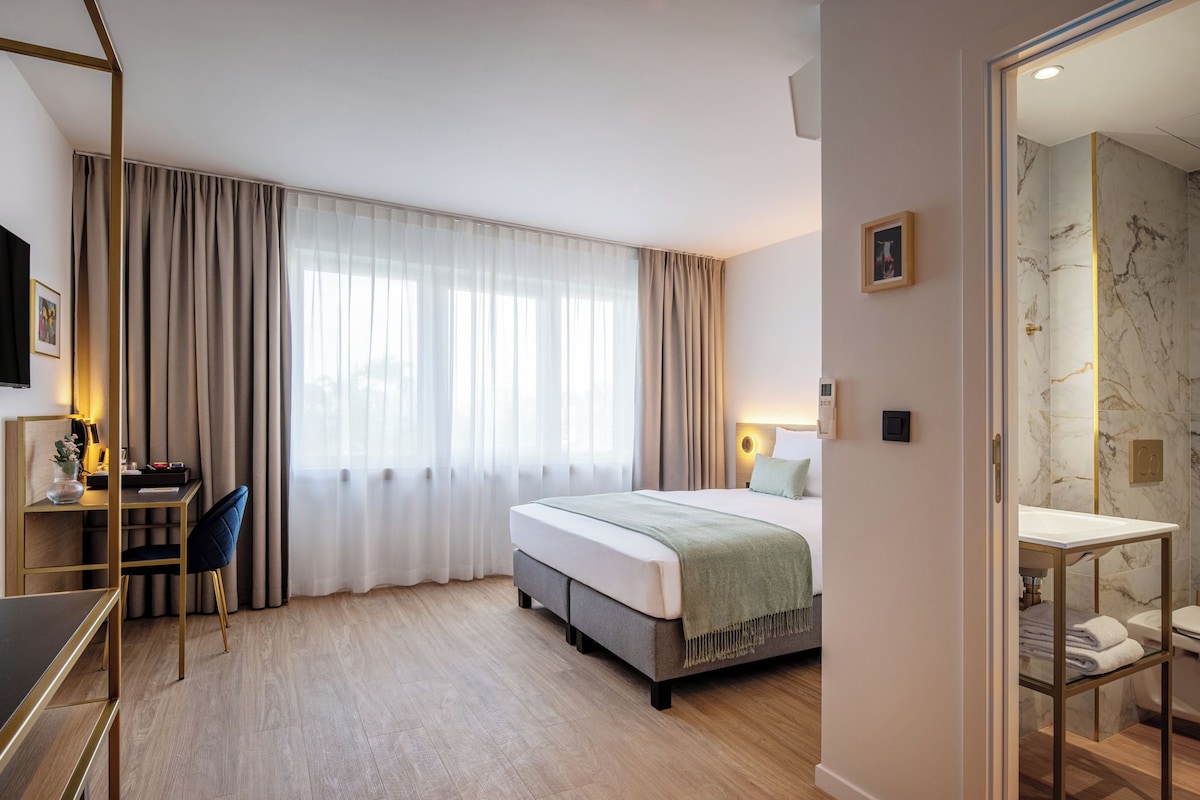 A hotel room with a bed, a desk with a chair, a TV, and a bathroom with a marble wall.