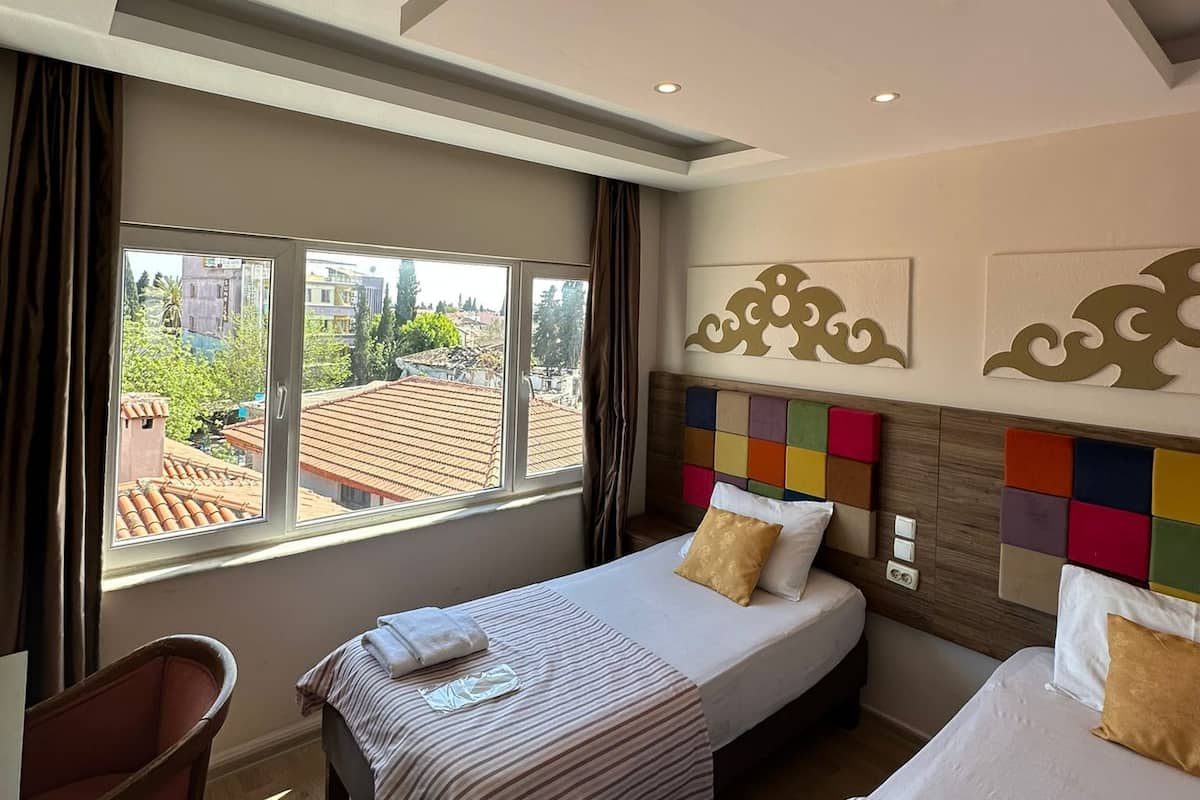 A hotel room with two beds, a view of the cityscape, and a modern ceiling design.