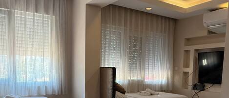 A hotel room with two beds, a flat-screen TV mounted on the wall, and a ceiling-mounted air conditioning unit.