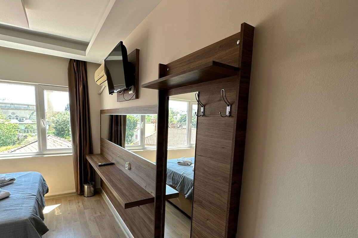 A bedroom with a bed, a wooden bench, a TV mounted on the wall, and a window with curtains.