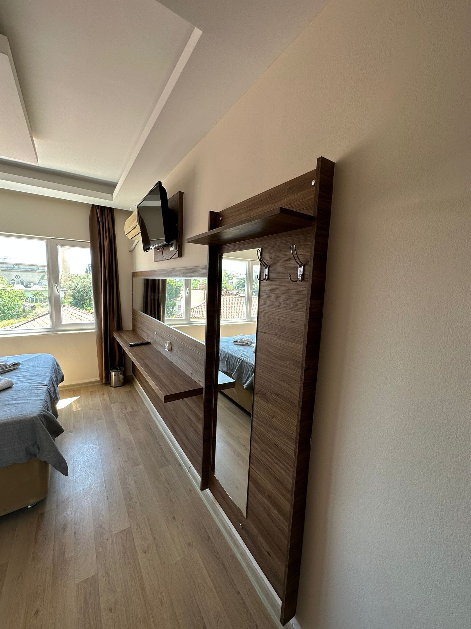 A bedroom with a bed, a wooden bench, a TV mounted on the wall, and a window with curtains.