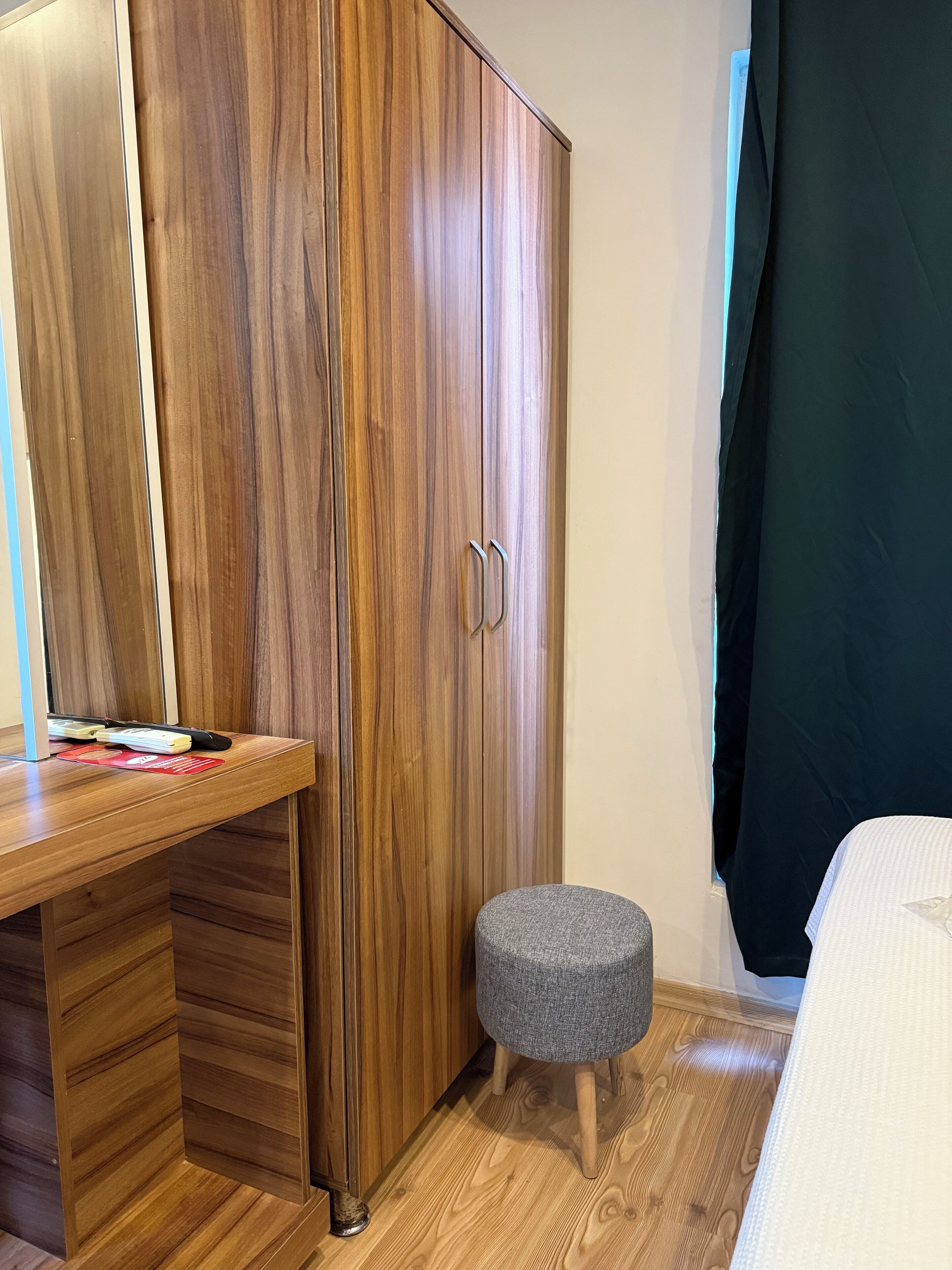 A bedroom with a wooden wardrobe, a small stool, and a bed.
