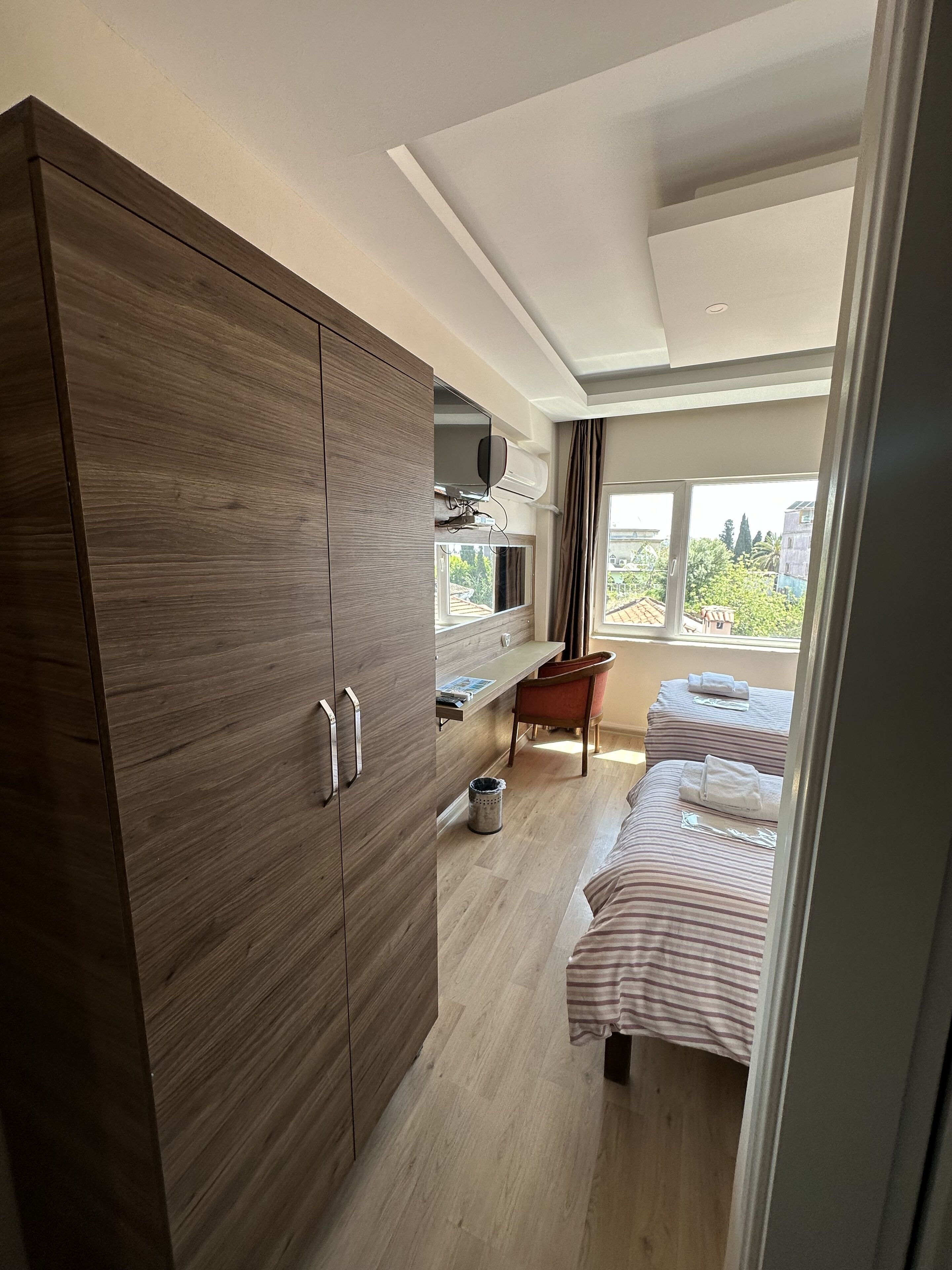 A modern bedroom with a wooden wardrobe, a small desk, a chair, and two beds with striped bedding.
