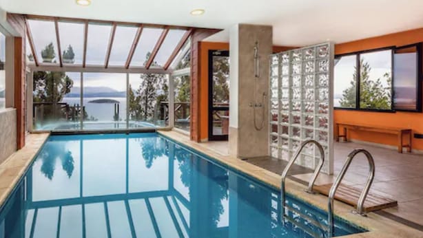 Una piscina interior moderna con paredes de vidrio transparente, vistas al mar y una zona de terraza de madera.