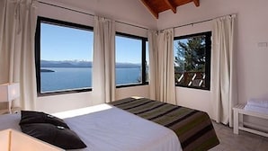 Un dormitorio con una cama grande, dos ventanas y vistas a un cuerpo de agua.