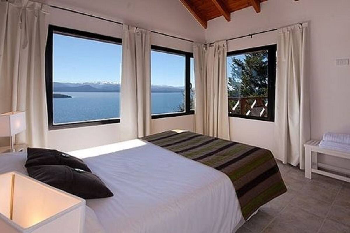 A bedroom with a large bed, two windows, and a view of a body of water.