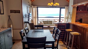 Un comedor con mesa y sillas, una encimera de cocina con taburetes, y vistas al exterior.