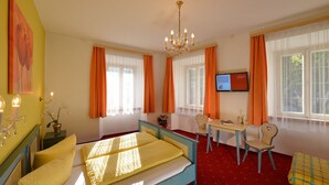 A bedroom with a bed, a desk, chairs, a TV, and a chandelier. - Gasthof Sonne (Imst)