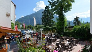 An outdoor café with tables and chairs, surrounded by greenery and a mountain in the background. - Gasthof Sonne (Imst)