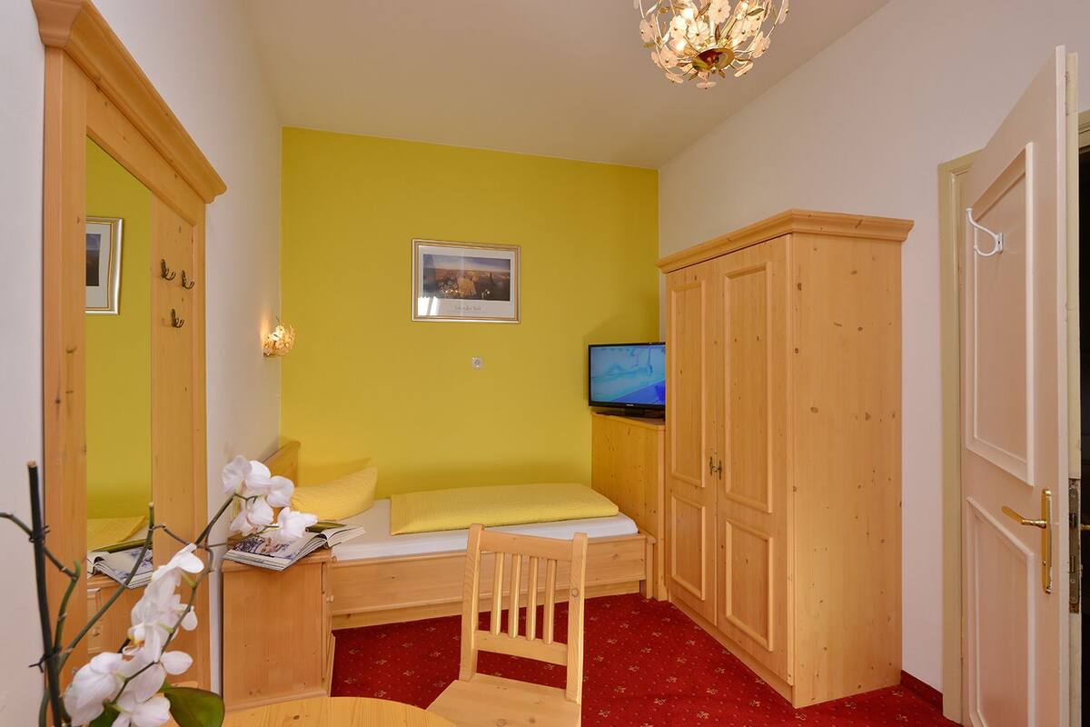 Ein kleiner Raum mit einem Bett, einem Fernseher, einem Kleiderschrank und einem Spiegel.
