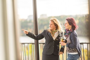 Two individuals standing by a railing, overlooking a body of water with a distant landscape.
