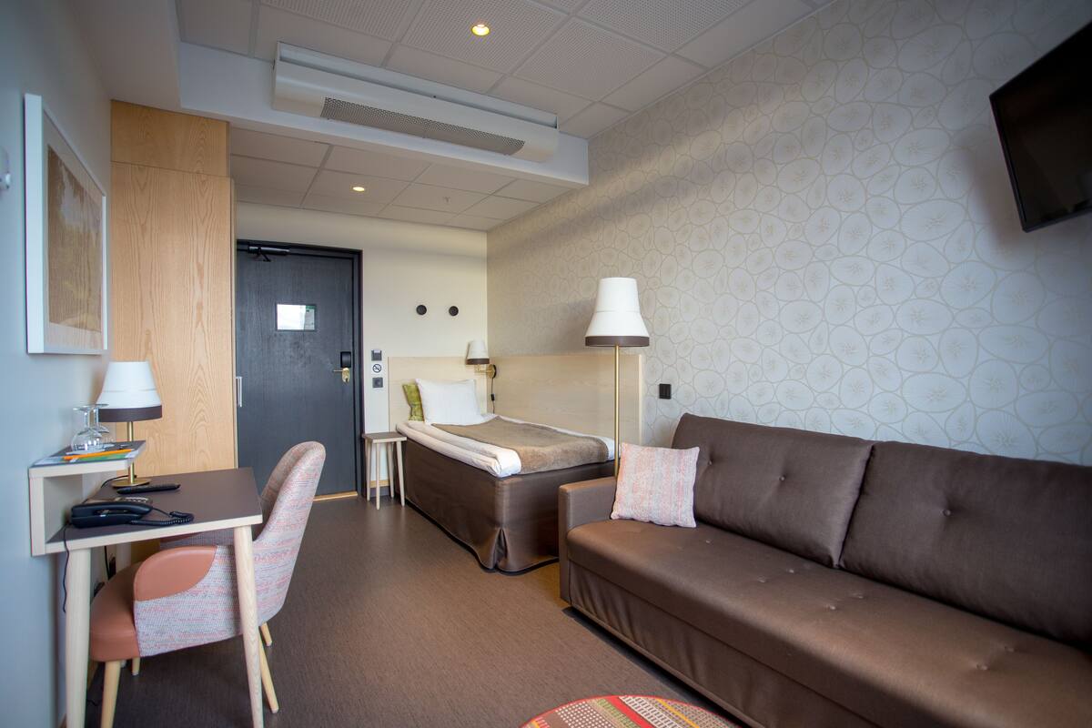 A hotel room with a bed, a sofa, a desk with a lamp, and a chair.