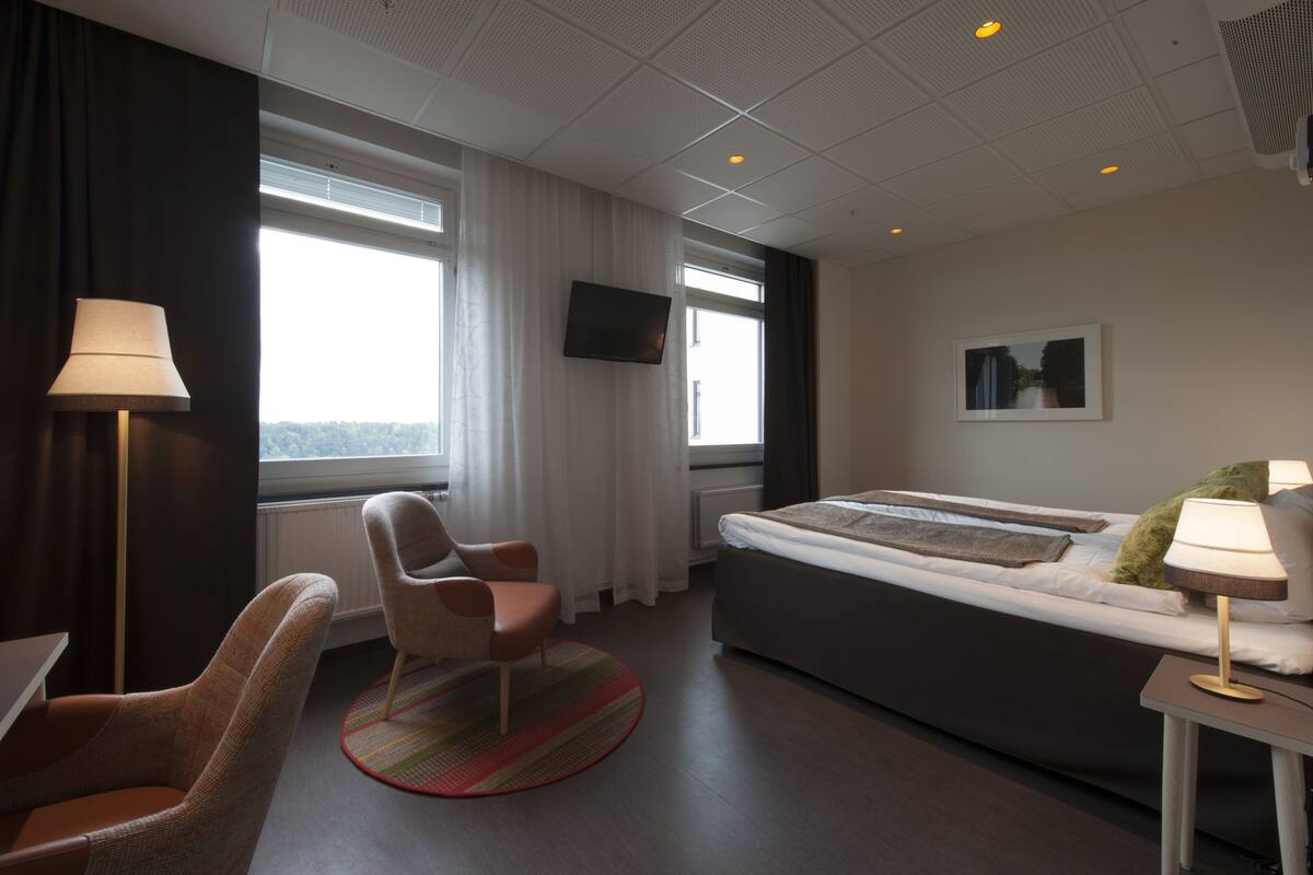 A hotel room with a bed, a chair, a desk, a TV, and a window with curtains.