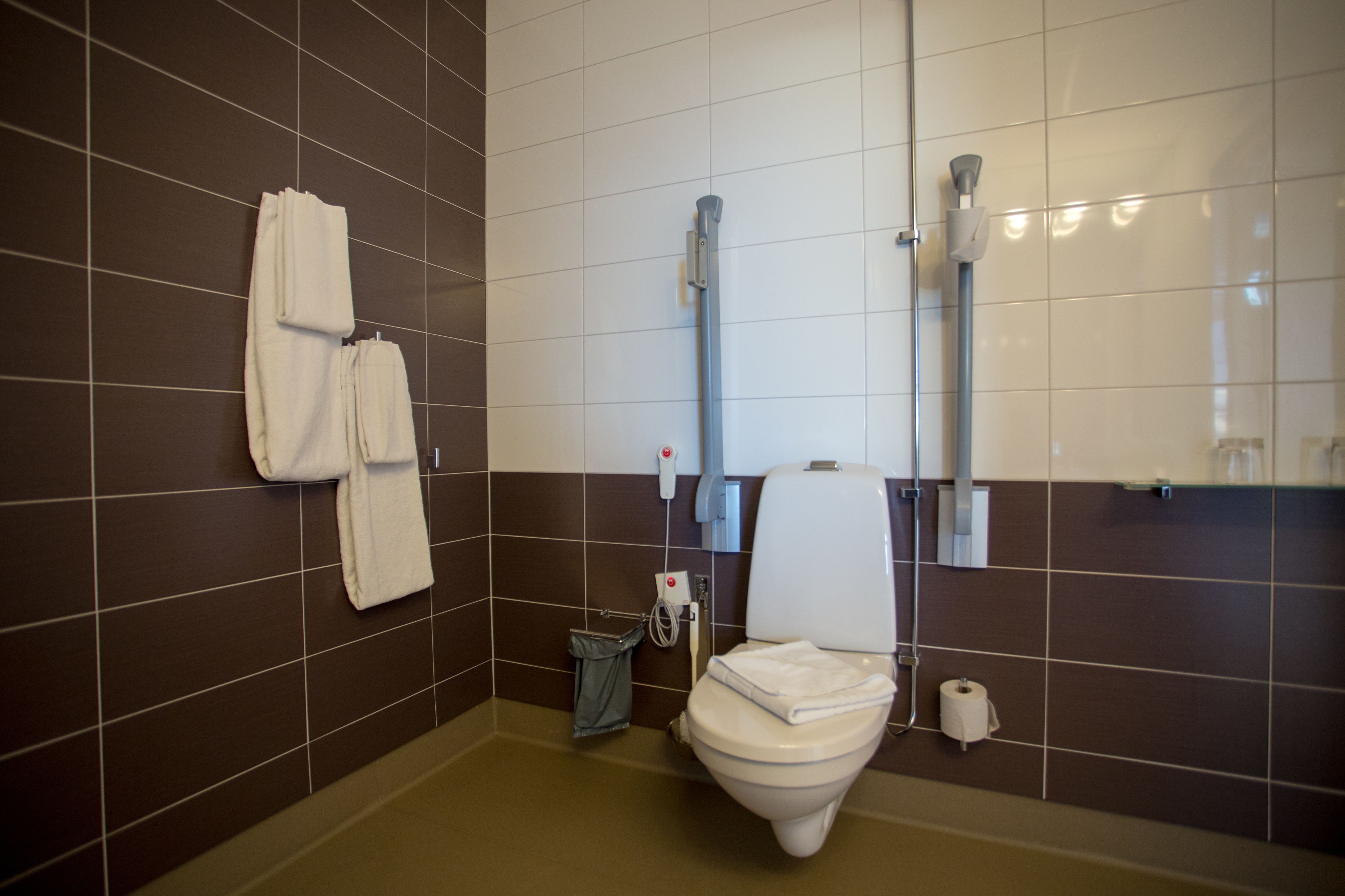 A bathroom with a toilet, a hand dryer, and a trash can.