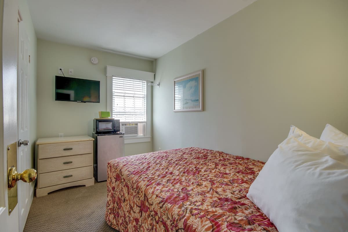 Un dormitorio con cama, cómoda, televisor y ventana con persianas.
