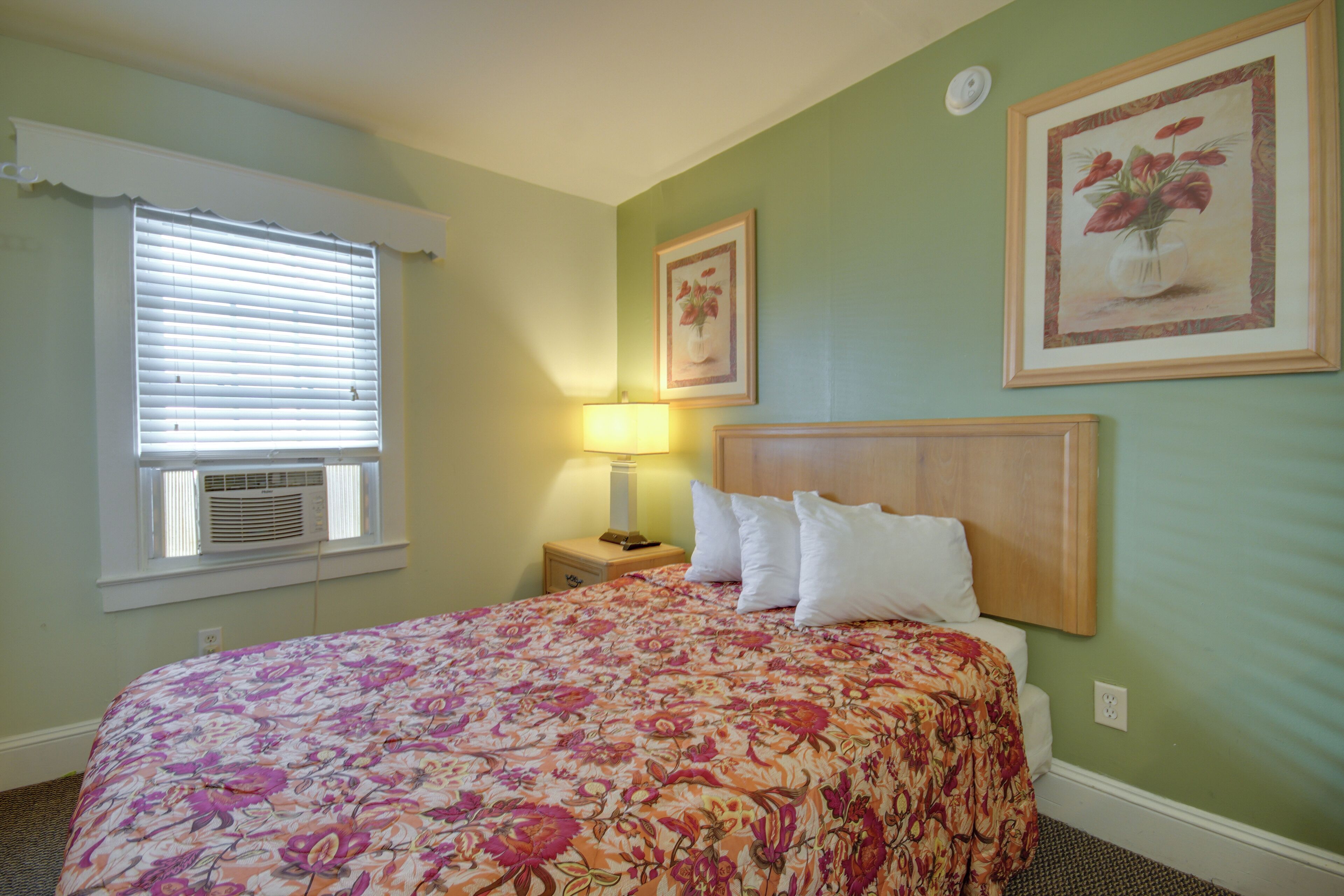 A bedroom with a floral bedspread, a bedside lamp, and two framed floral pictures on the wall.