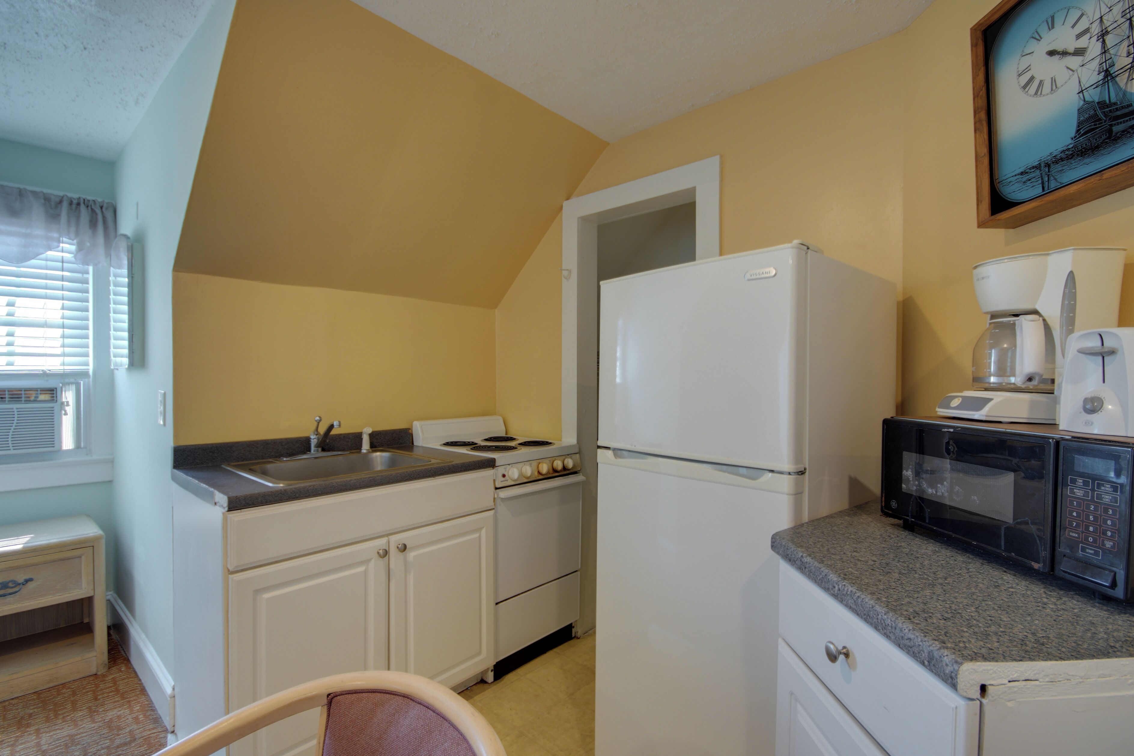 A compact kitchen with a sink, stove, refrigerator, microwave, and a coffee maker.