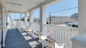 A covered porch with white railings and chairs, overlooking a street with buildings and parked cars. - Ocean Lodge Hotel South (Ocean City)