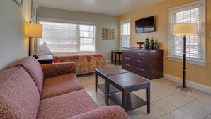 A compact hotel room with a sofa, a bed, a small table, a dresser, a TV, and a lamp. - Ocean Lodge Hotel South (Ocean City)