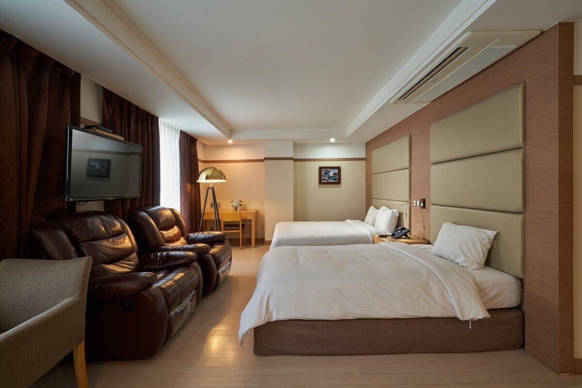 A hotel room with two beds, a leather sofa, a desk, and a TV.