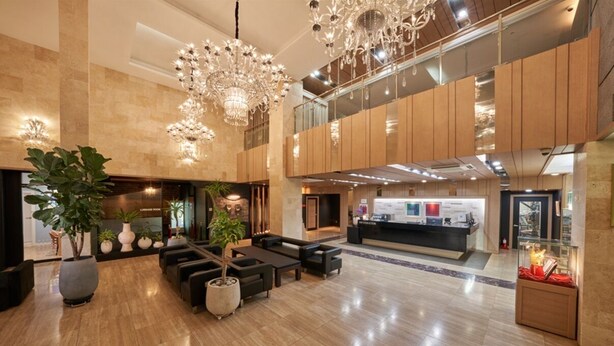 Un vestíbulo amplio con una recepción, zona de estar y grandes candelabros.