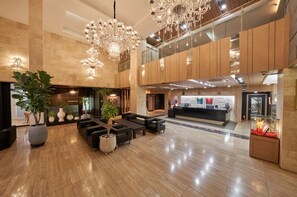 A spacious lobby with a reception desk, seating area, and large chandeliers.