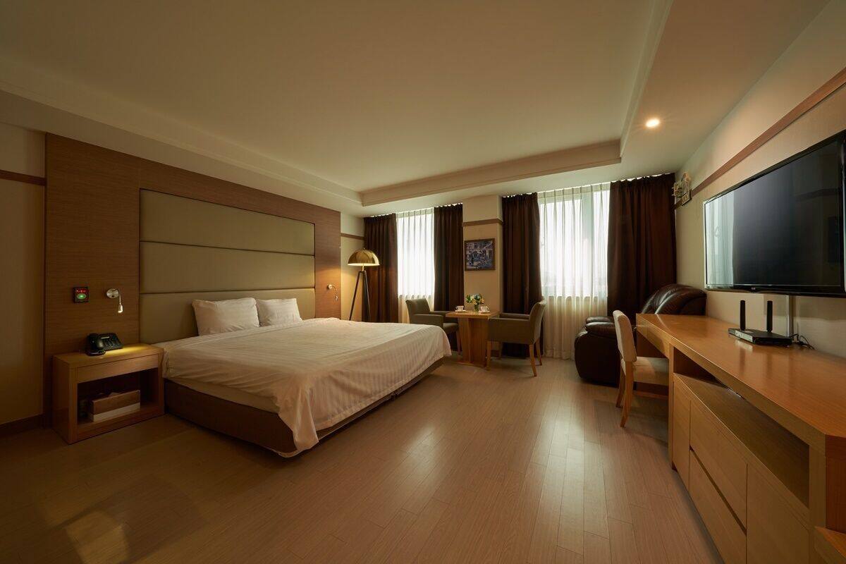 A hotel room with a bed, desk, TV, and seating area.