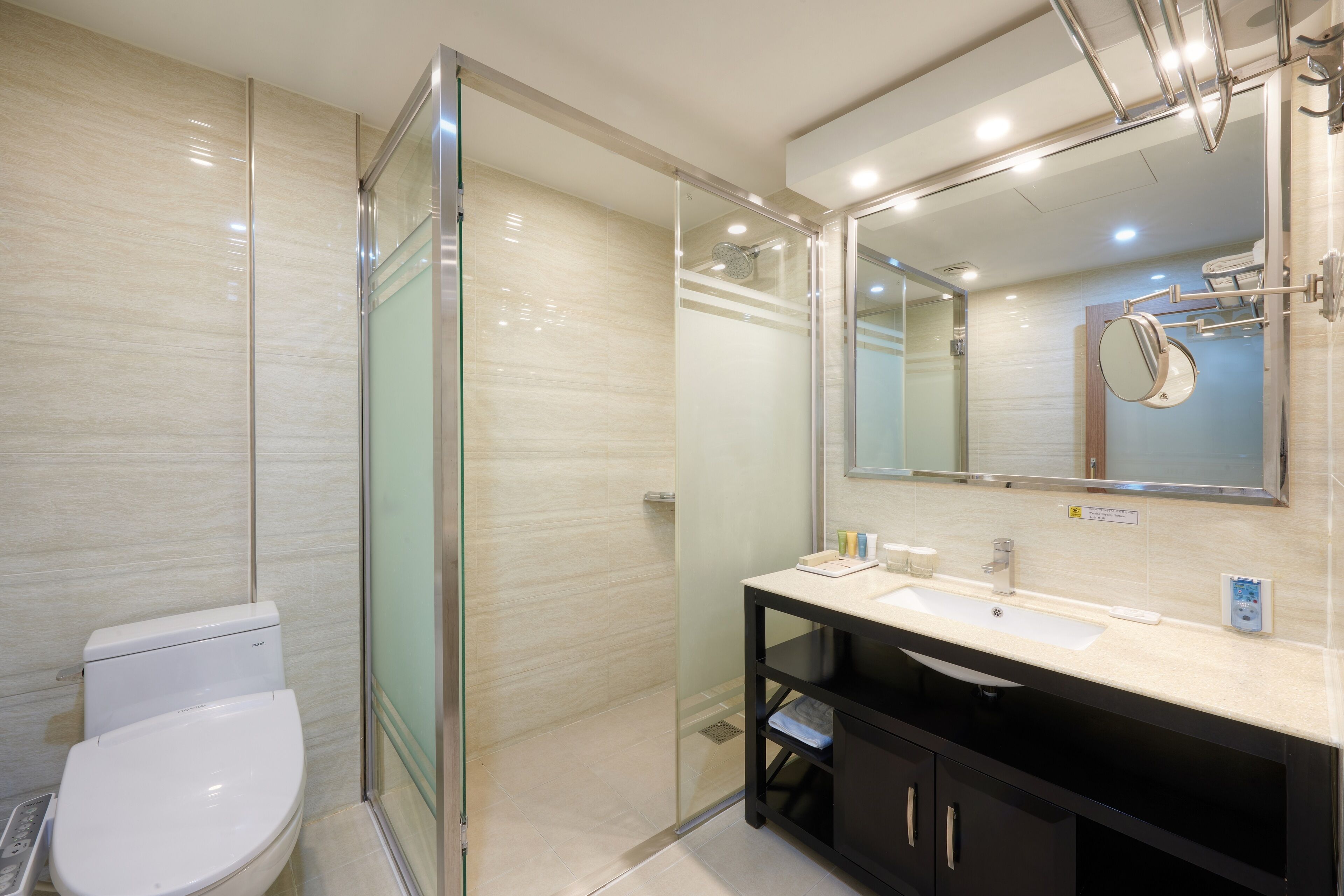 Une salle de bain moderne avec une douche à parois de verre, des toilettes blanches, un lavabo avec un miroir et un meuble noir.