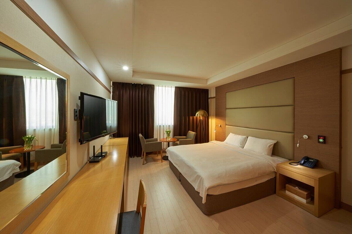 A hotel room with a large bed, a desk with a chair, a television, and a bedside table with a phone.