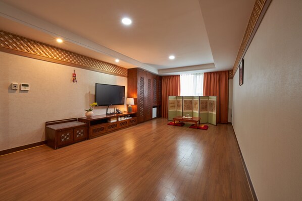 A spacious living room with a flat-screen TV, wooden furniture, and a traditional decorative screen.