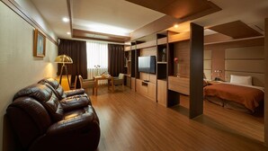 Una habitación de hotel moderna con sofá de cuero, zona de comedor, televisor y cama.