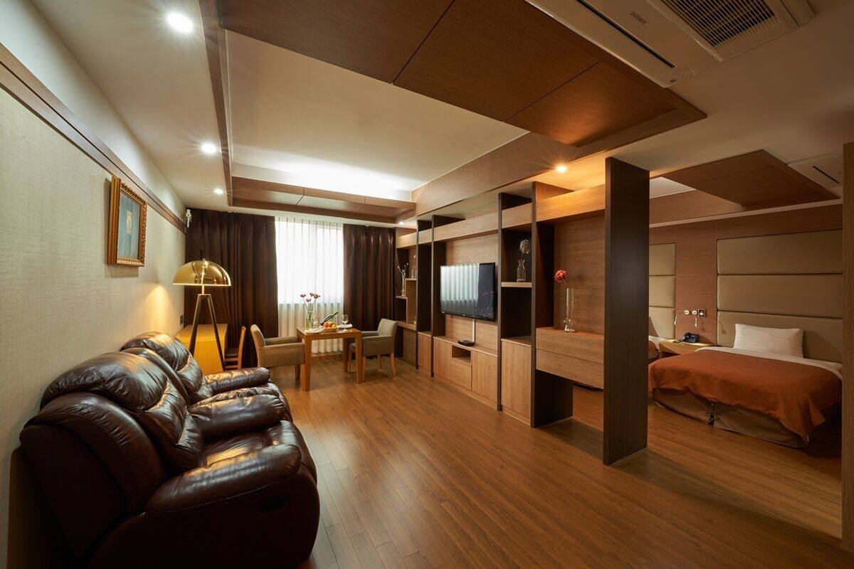 A modern hotel room with a leather sofa, a dining area, a TV, and a bed.