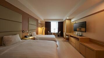 A hotel room with two beds, a desk, a chair, a TV, and a lamp.