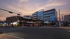 Un hotel moderno con un llamativo letrero que dice 'GG HOTEL', una intersección de calles y edificios urbanos circundantes.