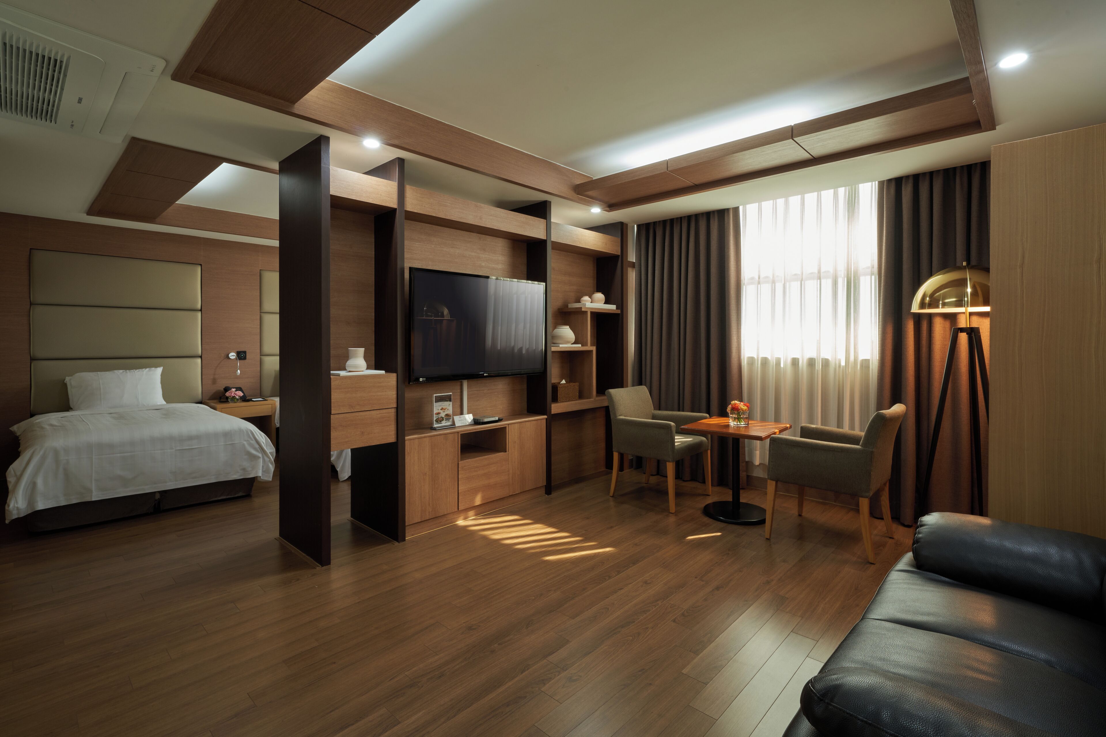 Ein modernes Hotelzimmer mit Bett, Fernseher, Schreibtisch, Sessel, Sofa und Lampe.