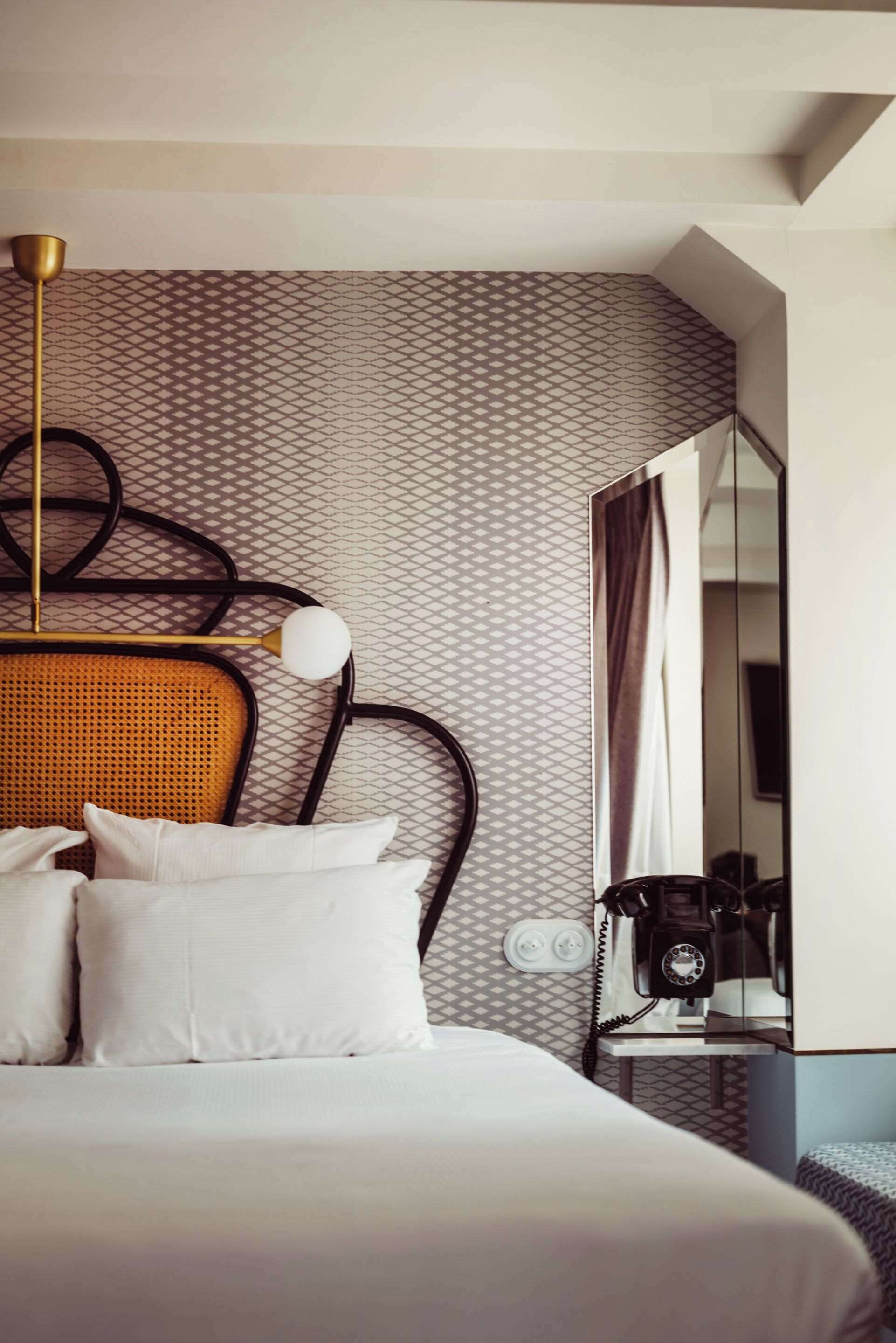 Une chambre d’hôtel comprenant un lit, une tête de lit, une table de chevet avec un téléphone et un mur orné d’un motif géométrique.