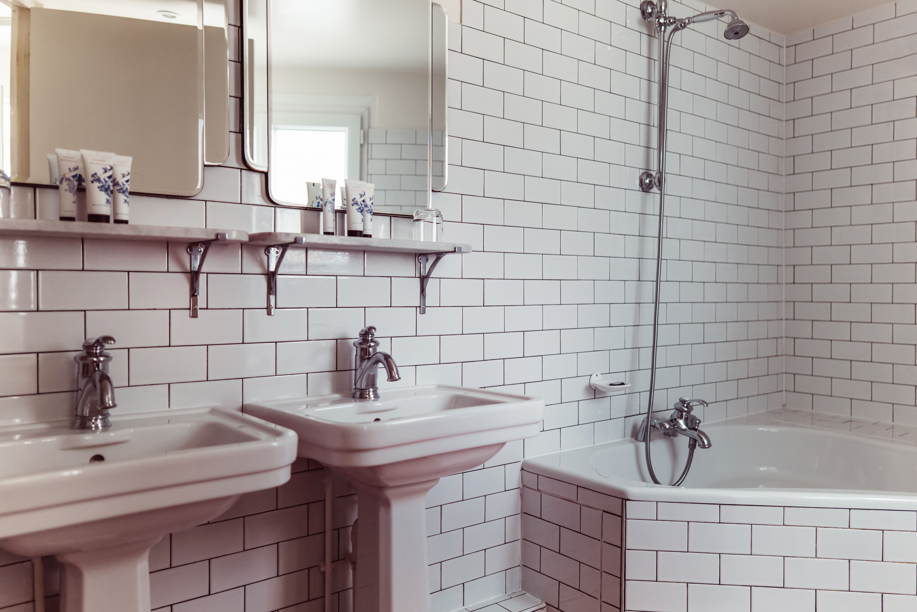 A bathroom with white tiled walls, two sinks, a mirror, and a bathtub.