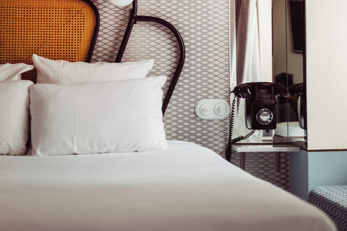 A hotel room with a bed, a headboard, a telephone, and a mirror.