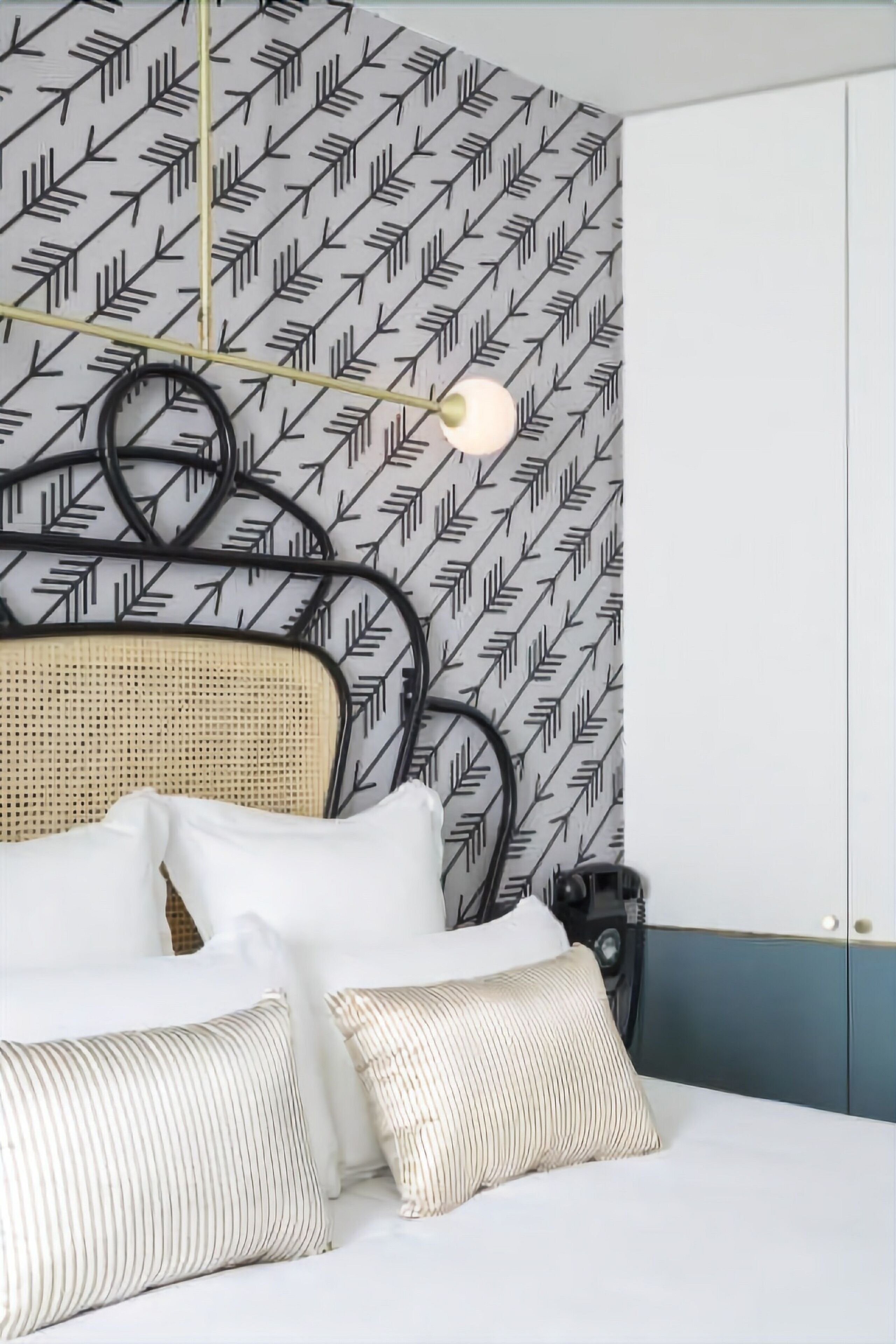 A bed with white bedding and striped pillows, a headboard with a woven design, and a wall with a geometric pattern.